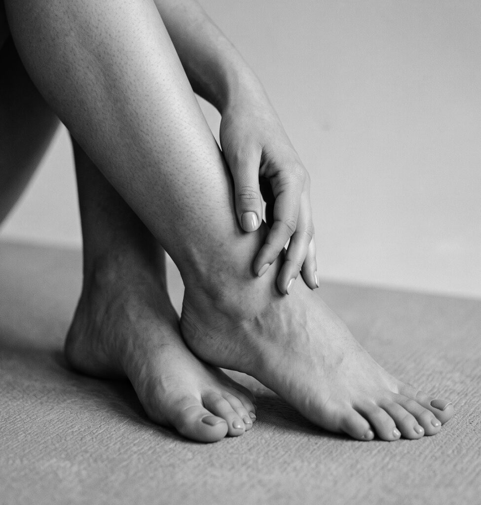 Mujer sentada y descalza sujetándose el tobillo con las manos