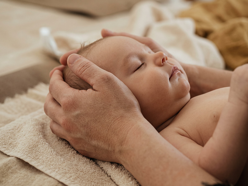 Bebé dormido mientras unas manos le sostienen la cabeza en una sesión de osteopatía